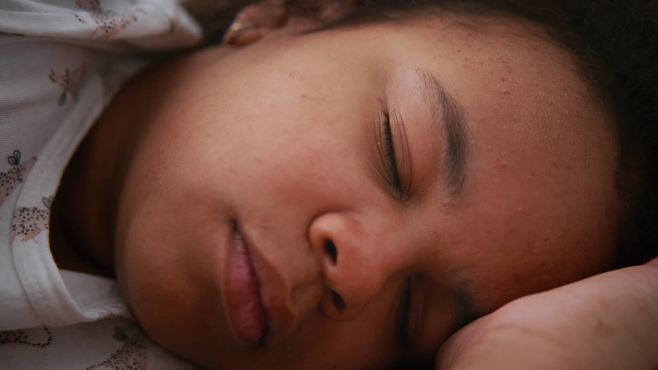 Young African American girl resting peacefully, lying on soft pillow with relaxed facial expression during quiet nighttime moment, embodying childhood serenity and comfort