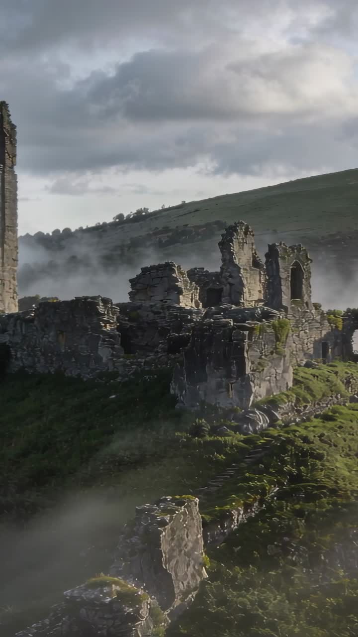 Video verticale: Telecamera che panoramica mostrando un castello in rovina su un pendio erboso, rivelando una torre e degli archi.