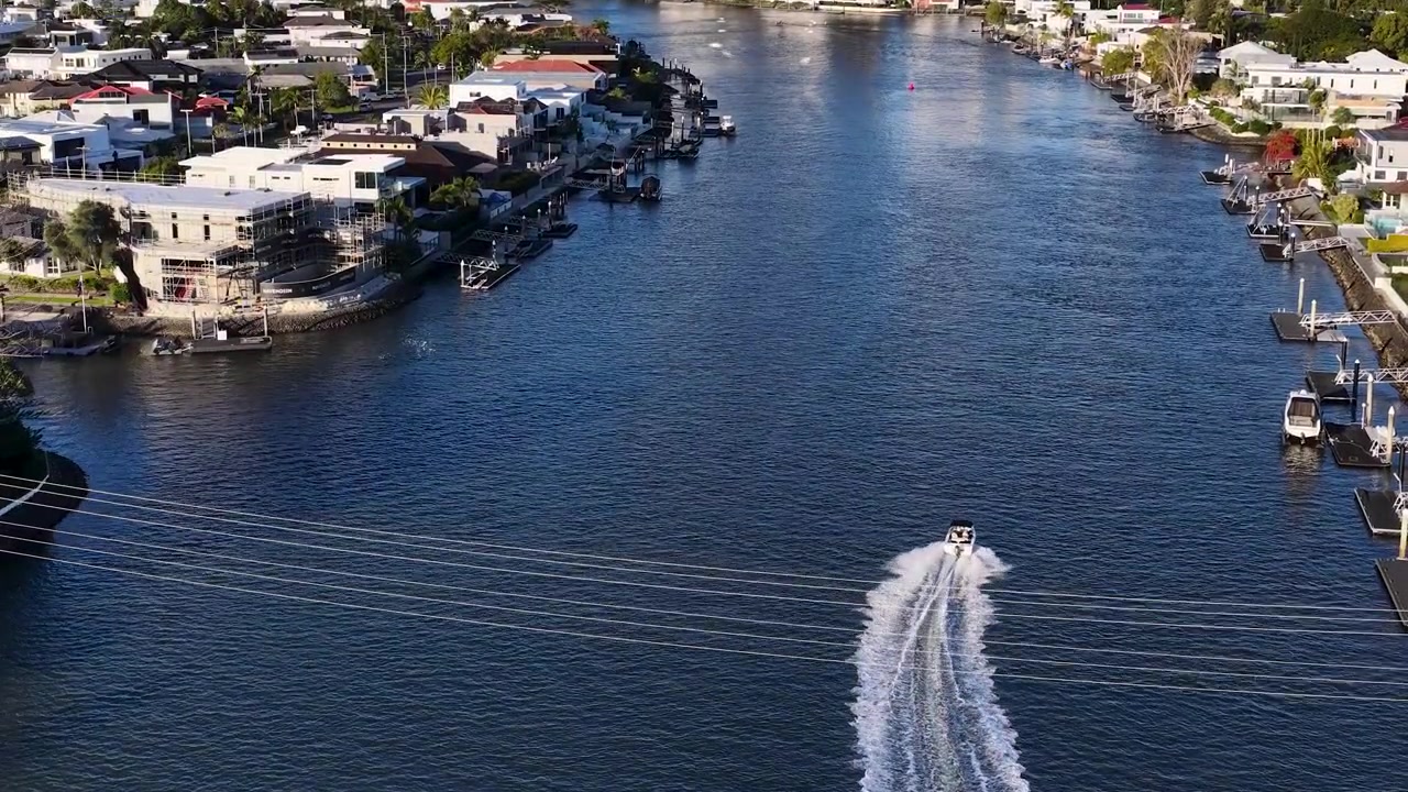Ripresa aerea con drone dall'alto di un motoscafo bianco che viaggia attraverso un canale navigabile residenziale illuminato dal sole.