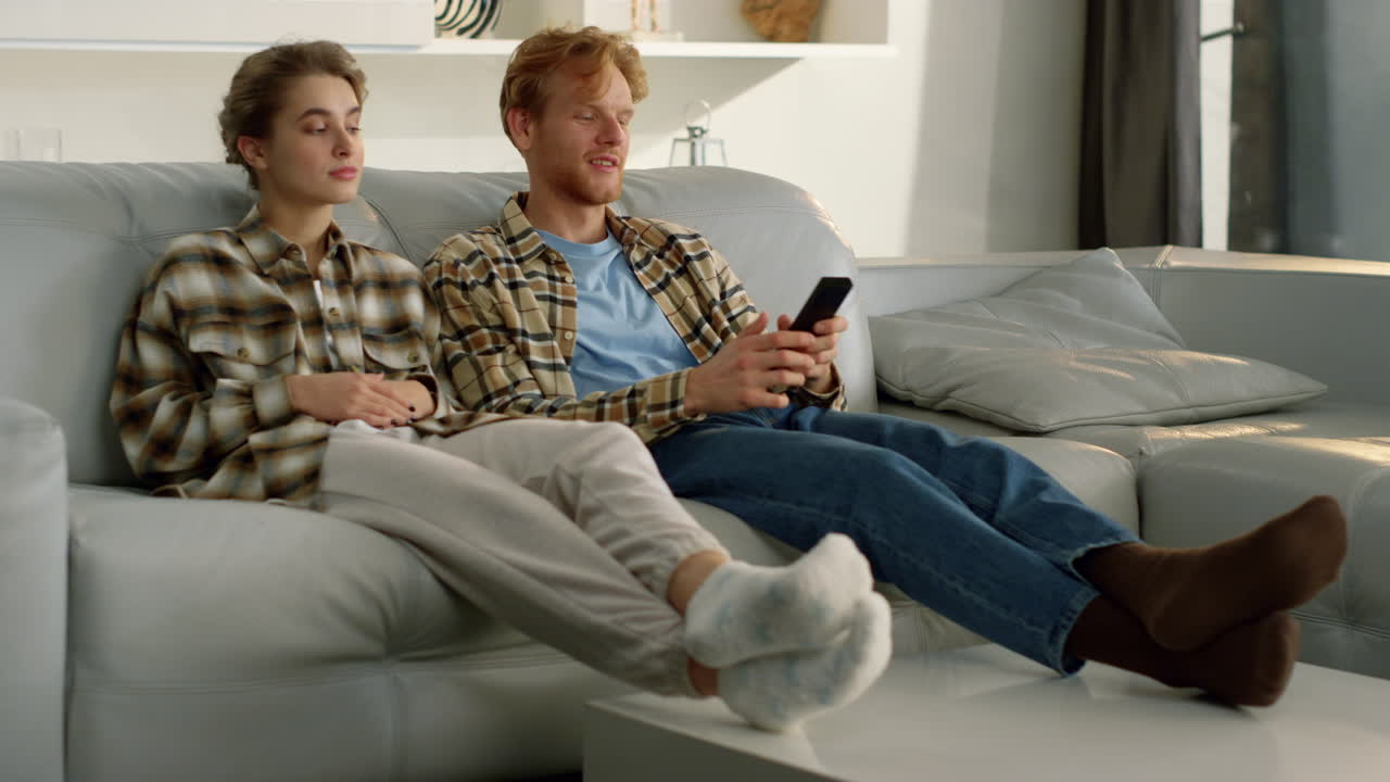 pareja casada descansando en el sofá juntos. marido pelirrojo cambiando de canal de televisión