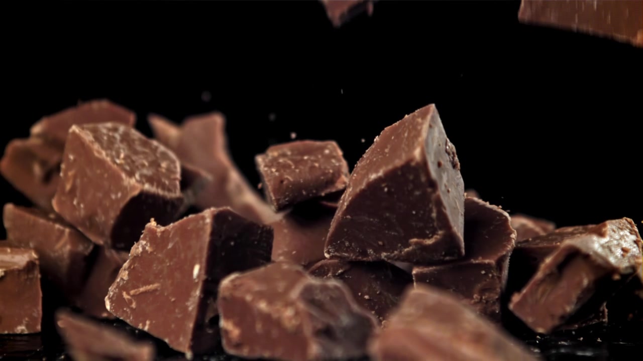 Movimento rallentato: pezzi di cioccolato che cadono su sfondo nero.