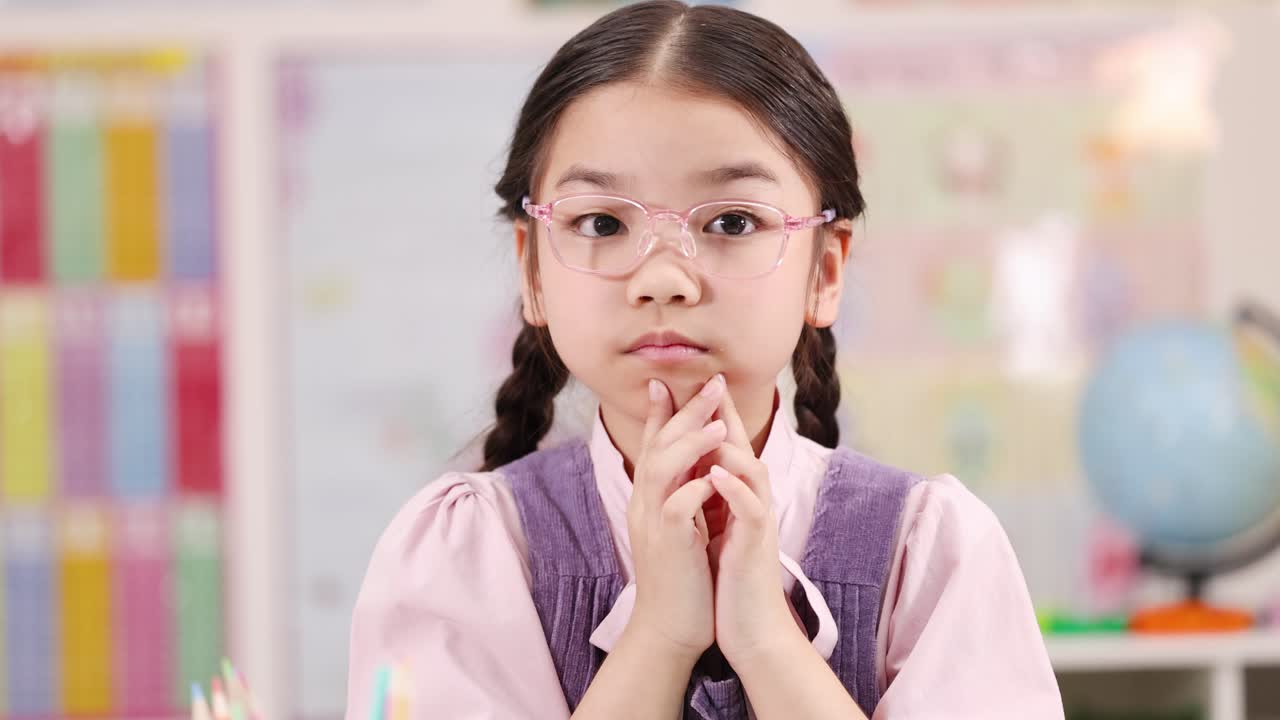 Young girl in glasses shakes head, signaling no, in brightly lit classroom environment