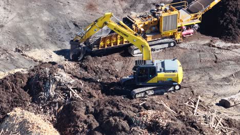 drone captures excavator and tractor moving soil and mulch in a construction site under bright daylight