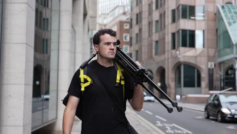 Young-man-is-walking-central-London-with-his-camera-and-tripod