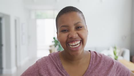 Portrait-of-smiling-african-american-plus-size-woman-looking-at-camera-and-laughing-in-living-room