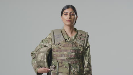 studio portrait of serious young female soldier in military uniform against plain background