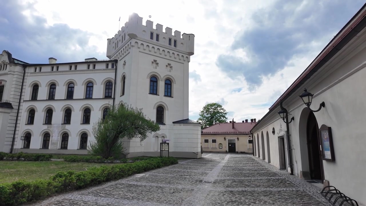 Una torre bianca si erge sopra il complesso medievale, affiancata da mura residenziali sulla sinistra e una stalla sulla destra