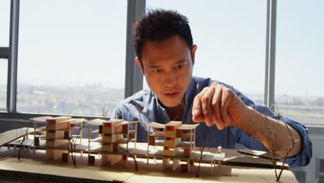 Front-view-of-Asian-male-architect-looking-at-architectural-model-in-a-modern-office-4k