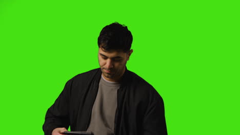 Young-Man-Getting-Alert-And-Looking-At-Text-Message-On-Mobile-Phone-Standing-Against-Green-Screen