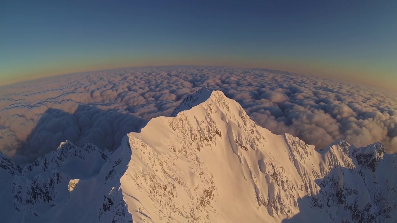 Veduta aerea di una vetta montuosa innevata sopra le nuvole al tramonto