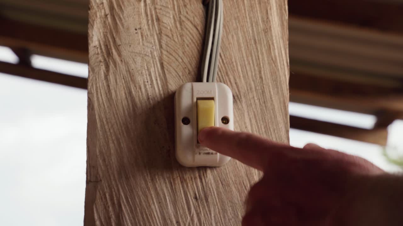 K HD cinematic close-up shot of a hand turning a white light switch on and off, mounted on a rustic wooden beam. interaction with the switch, texture of the wood and the modern white switch
