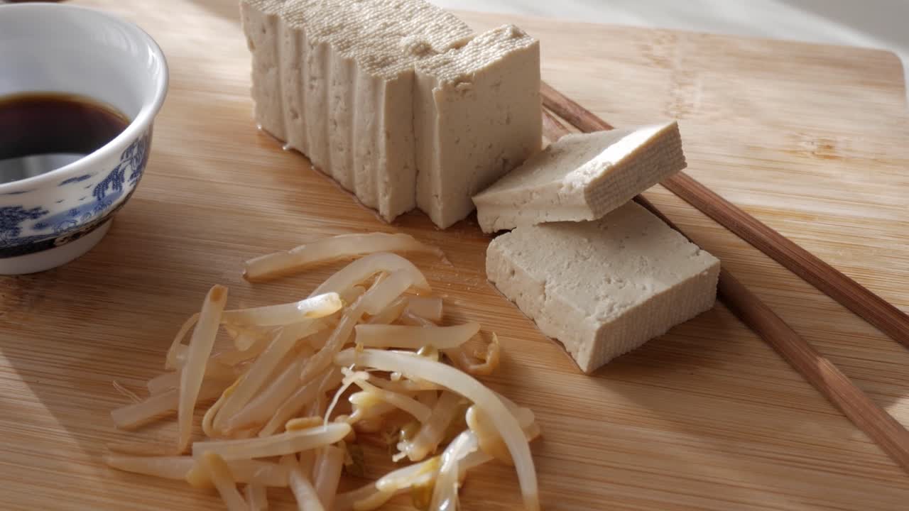 Tofu slices on wood table with soy sauce, minimal food scene, top view, natural light