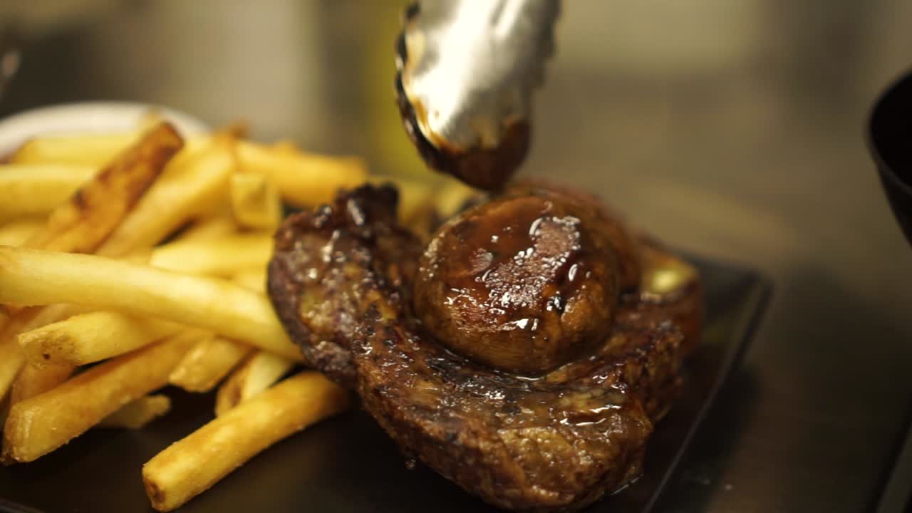 cámara lenta - primer plano - terminando la presentación de filete de ternera a la parrilla, salsa, champiñones, papas fritas doradas y ensalada verde en un plato negro