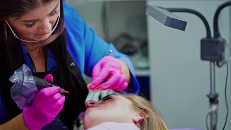 beauty spa. young cosmetologist doing permanent make-up tattoo on patient's lips. professional tattooist making permanent make-up. cosmetology concept.