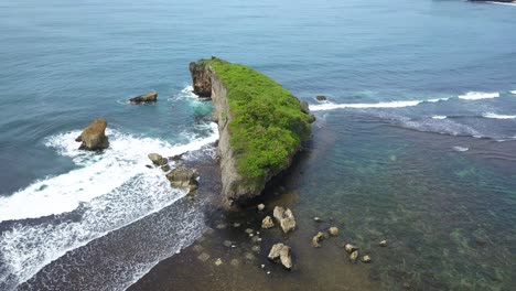 Drone-shot-of-coral-rock-on-the-beach-crashing-by-the-wave-with-clear-blue-sea-water