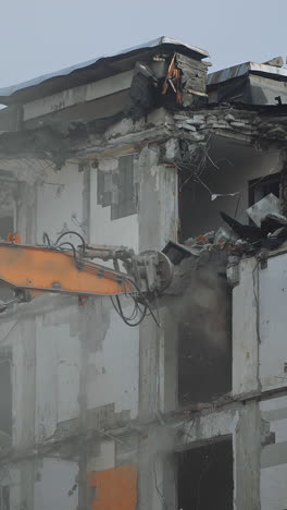 a scoop of demolishing machine breaks off the floors of the destroyed house. excavator working in the cloud of dust . vertical video