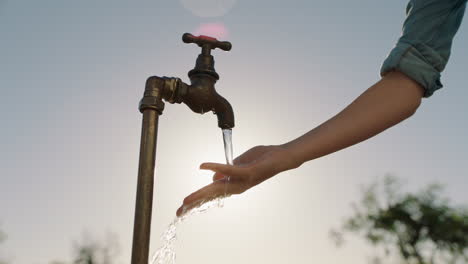 Bäuerin-Wäscht-Sich-Die-Hände-Unter-Leitungswasser-Auf-Einem-Ländlichen-Bauernhof-Mit-Süßwasser,-Das-Aus-Dem-Wasserhahn-Fließt,-Während-Die-Nachmittagssonne-Aufflackert