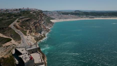 Drohnenaufnahme-Des-Leuchtturms-Von-Nazaré-Und-Blick-Auf-Die-Stadt-Aus-Der-Ferne