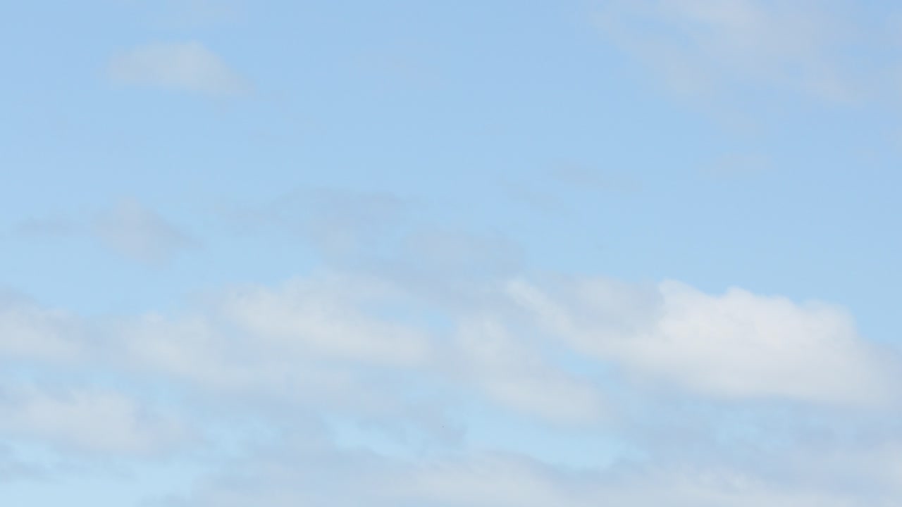 Soft white clouds move slowly in a bright blue sky, natural daylight, steady camera