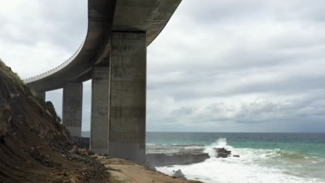 drone volando entre los pilares debajo del puente del acantilado marino en australia