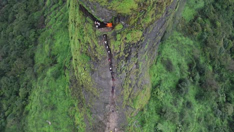 drone shot of ancient harihar fort with tourists climbing down steep and vertical stairs during monsoon trek, harshewadi, nashik, maharashtra, india