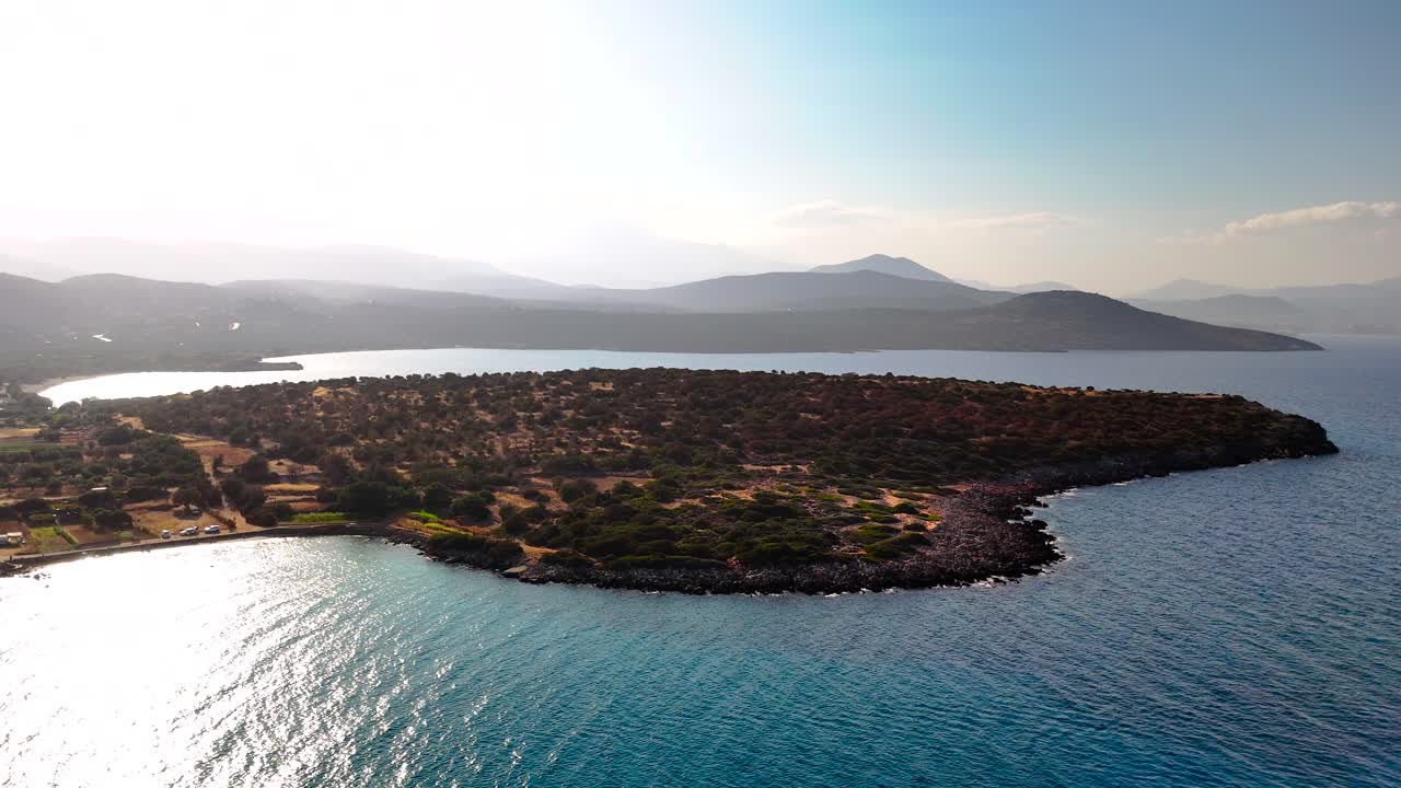 This captivating aerial shot showcases a peaceful island encompassed by clear blue waters as the sun sets, illuminating the surrounding landscape and softening the scenery