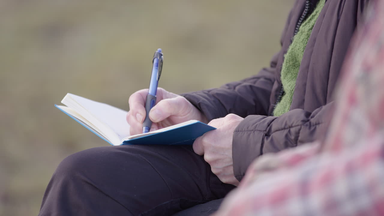 Elderly woman takes notes in journal during group therapy session, shallow focus