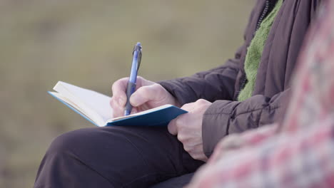 Elderly-woman-takes-notes-in-journal-during-group-therapy-session,-shallow-focus