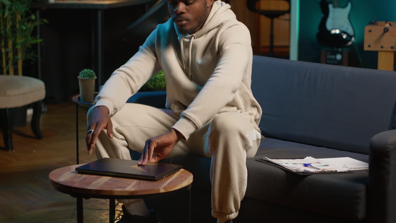 African american male freelancer managing creative projects remotely in his loft, working on a new novel or script for his gig. Man focusing on writing and editing creation, telework. Camera A.