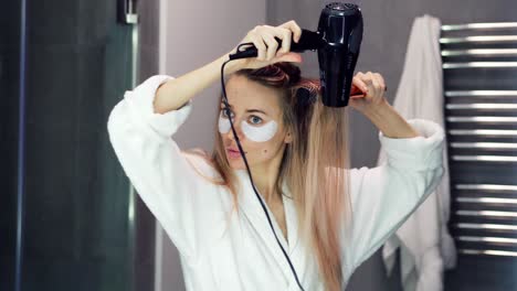 Woman-with-eye-patches-drying-her-hair-with-hair-dryer-and-brush