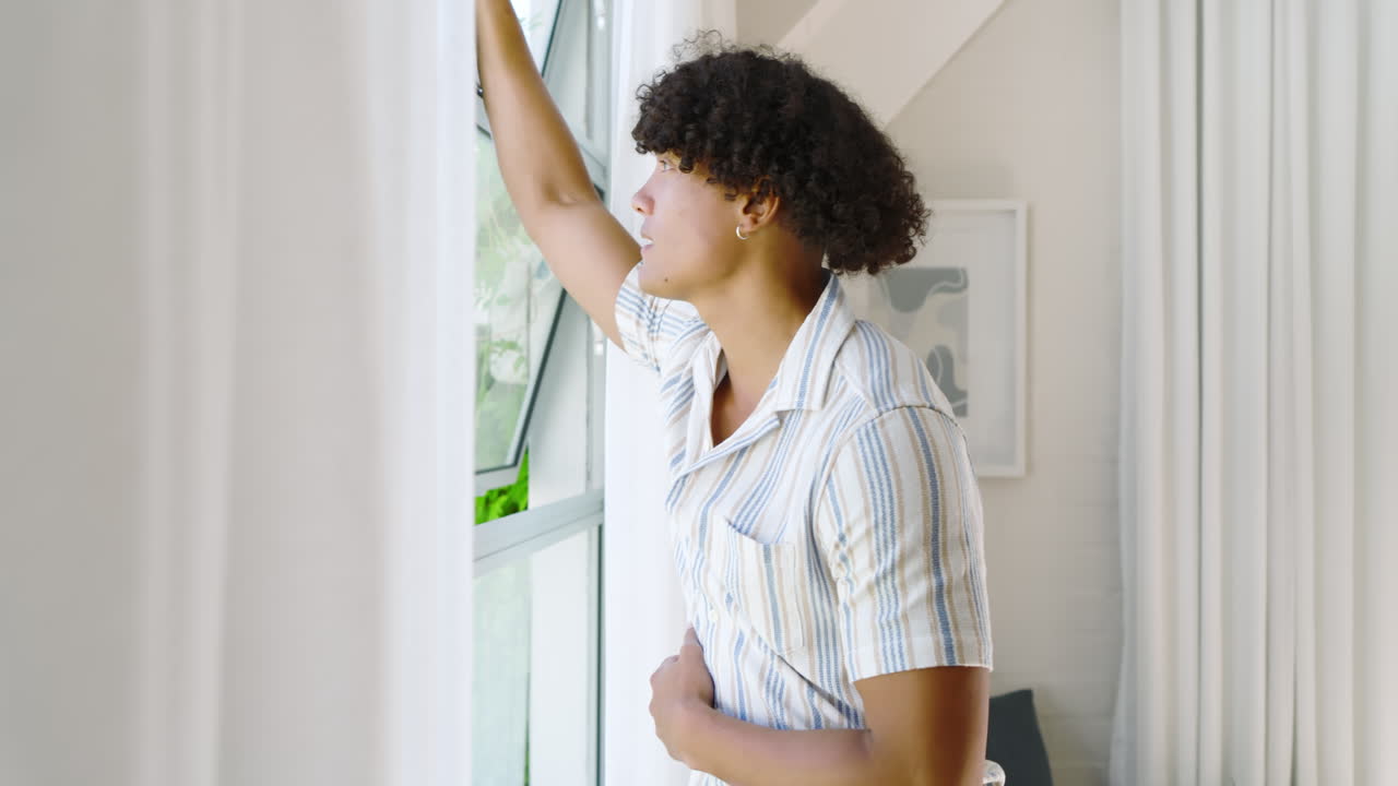Smiling young man in striped shirt enjoying fresh air by open window, at home