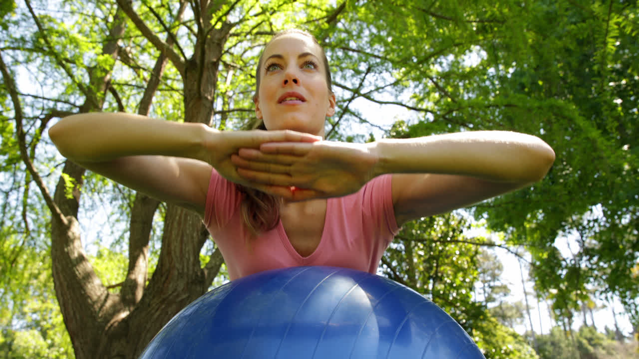 Donna in forma che fa esercizi per il core con la palla da fitness nel parco