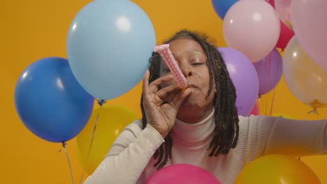 retrato de estudio de una mujer con una cinta para la cabeza de cumpleaños celebrando con globos y soplador de fiesta 2