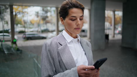 Ernsthafte-Geschäftsfrau,-Die-Auf-Der-Straße-Nachrichten-über-Ihr-Smartphone-Sendet.-Konzentrierte-Frau-Tippt-Handy