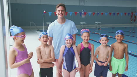 portrait of children standing by edge of swimming pool with male coach for lesson