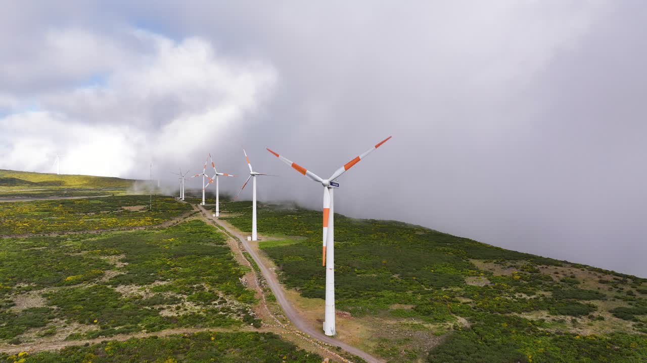 Turbine eoliche rotanti in cima a una montagna rigogliosa vicino a una coltre di nebbia a Madeira, Portogallo