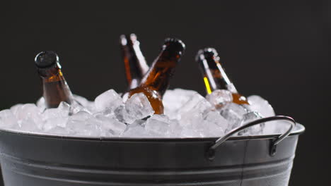 cerrar las botellas de vidrio de cerveza fría o refrescos que se enfrían en un cubo lleno de hielo contra un fondo negro