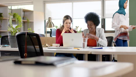 Happy-diverse-female-creative-colleagues-in-discussion-using-laptop-in-office,-slow-motion