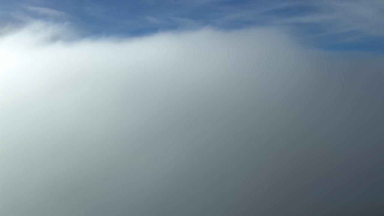 En fordybende cockpitudsigt under nedstigning i et endeløst hav af bløde skyer under en blå himmel