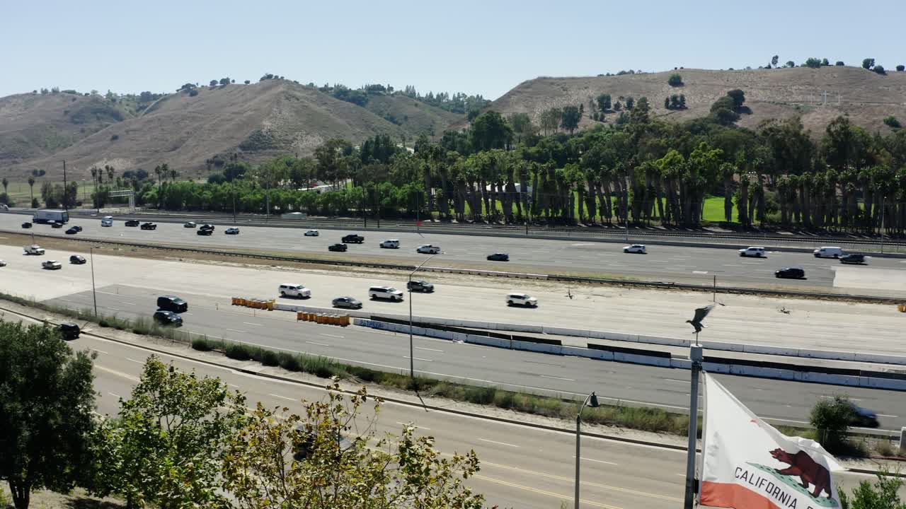 Drone shot of cars driving on the freeway with the California flag waving in the wind.