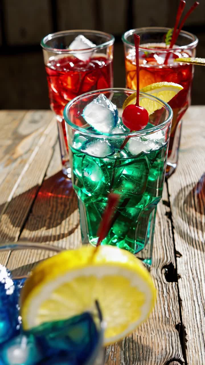Colorful cocktails with ice and fruit garnishes on a wooden table, captured from a high angle