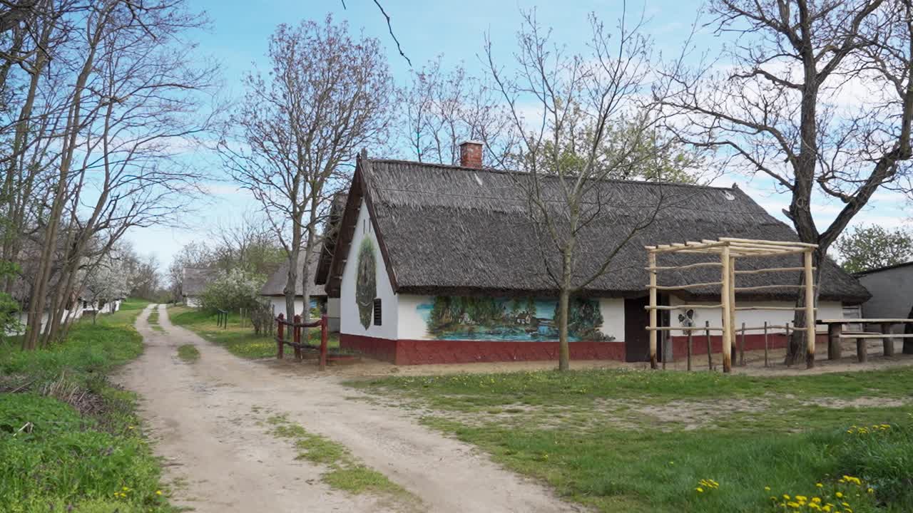 Maison traditionnelle au toit de chaume avec des murs peints le long d'un chemin de terre au printemps