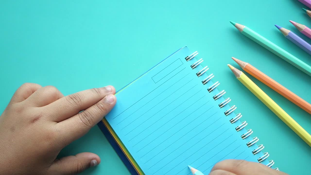 Child Writing in a Notebook with Colored Pencils