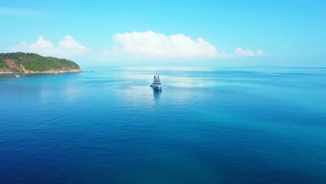 luxurious yacht sailing on calm blue water of lagoon near shore of tropical island on bright sky with white clouds background in thailand