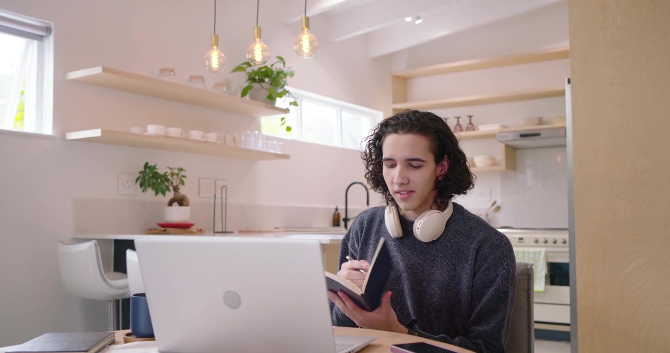 Homem afro-americano gesticulando em uma chamada de vídeo no laptop, depois pegando um caderno e fazendo anotações