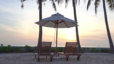 close-up of two empty lounge chairs and shade umbrella on the beach as the light from the sunset fades