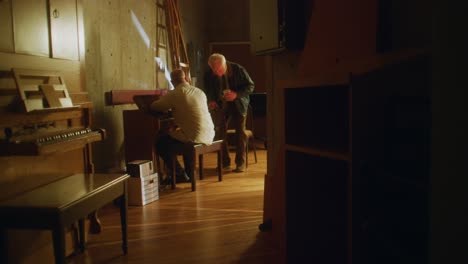 man sits at piano in hallway and is joined by a friend