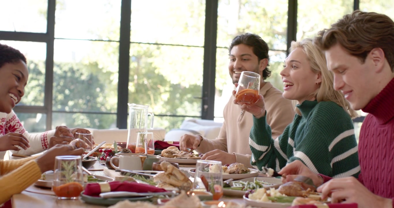 Diverse group laughing toasting sharing plates at table as African woman holding ornament Christmas