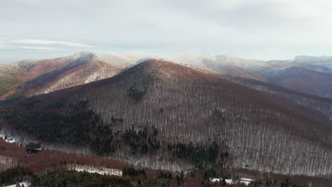 aerial push in towards tree-lined mountain peak, covered with light snow