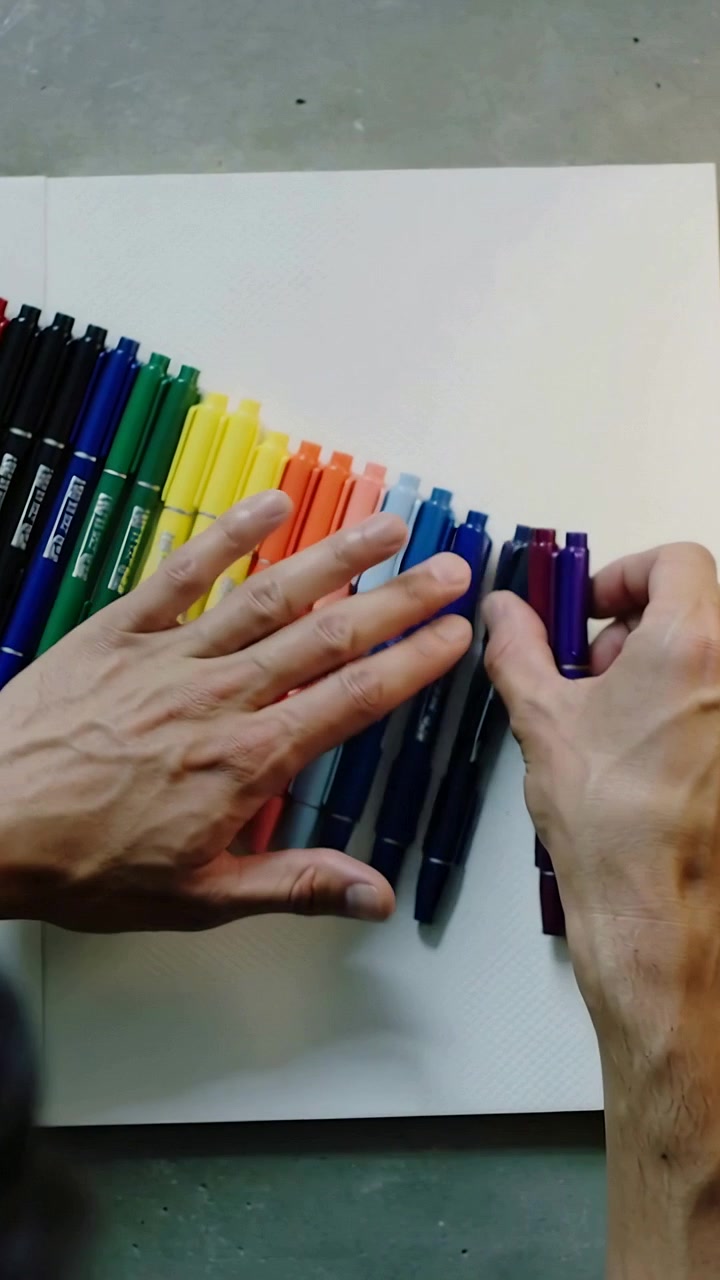 Vertical video: Picking up purple marker, artist hands arranging markers on sketchbook for drawing